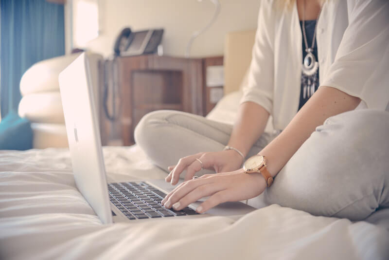woman sitting in bed typing on a macbook