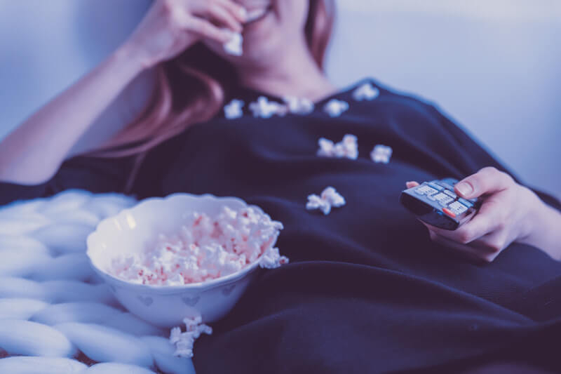 blond woman eating popcorn and holding a tv remote control in hands
