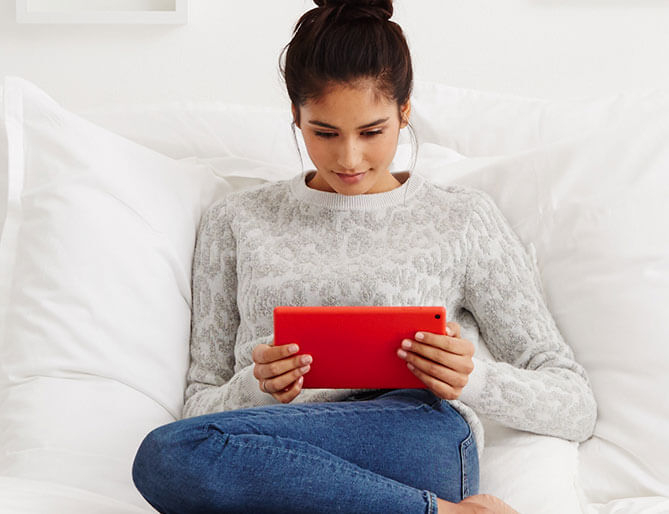 woman sititng on a couch holding a fire tablet in hands