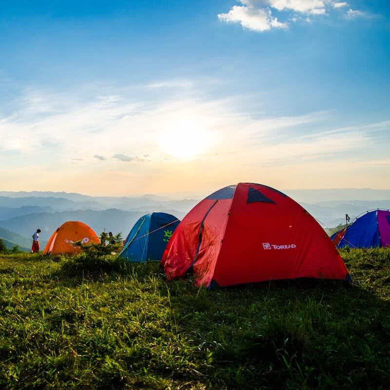 Red, blue and orange tents on grassy hillside